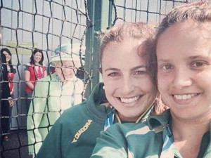 The Queen standing behind a net fence smiling in the direction of the camera, as Jayde Taylor, a member of the Australia Commonwealth Games hockey team, took a selfie with one of her teammates.
